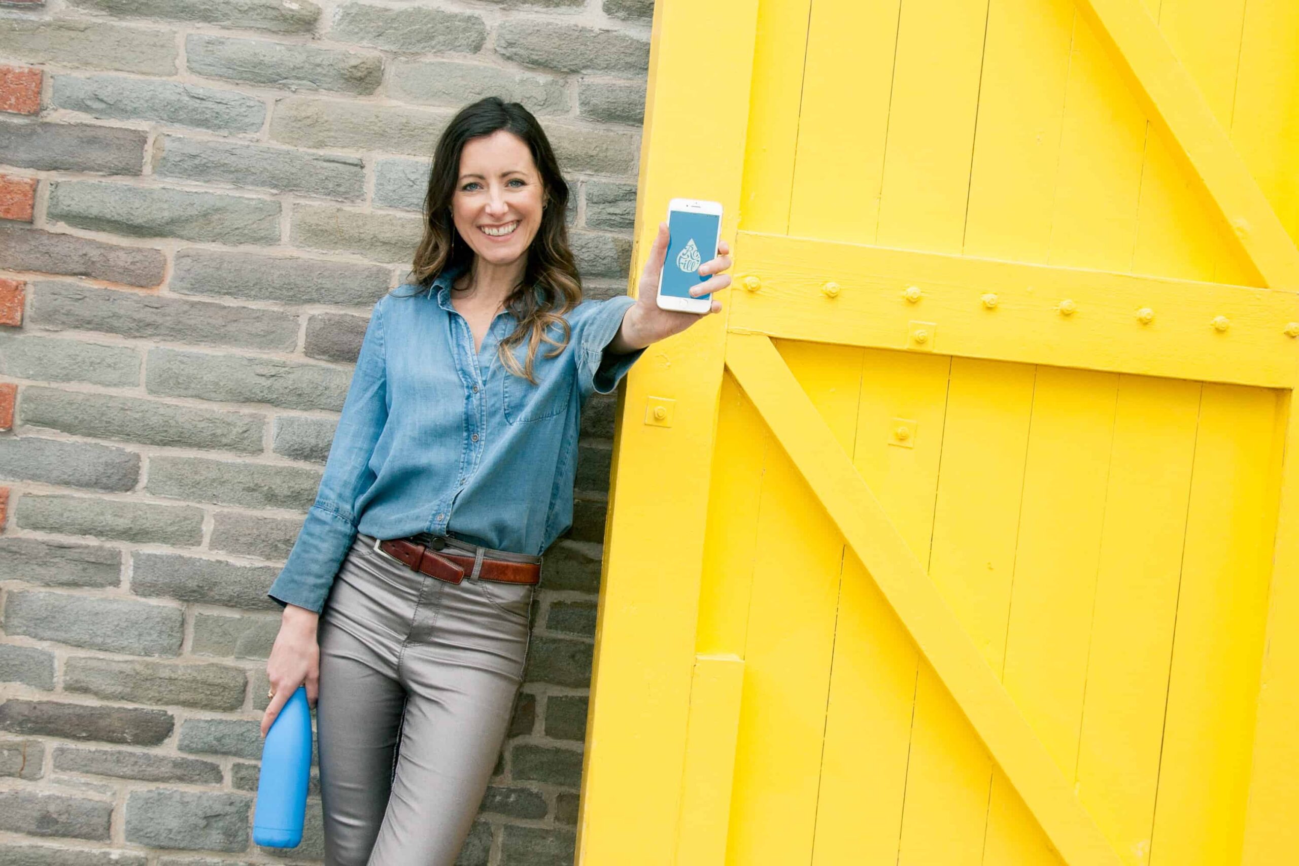 Women holding a cell phone in front of yellow door to celebrate Diags Shift app launch for job seekers